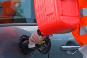 man in orange safety vest pouring gas into a car from a red gas plastic can
